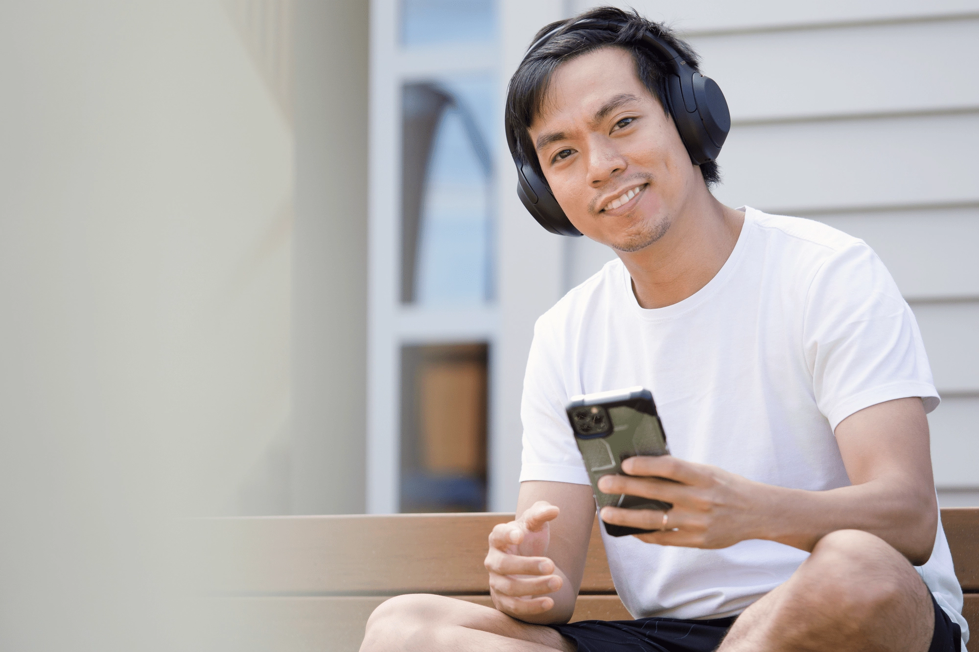 Man_smiling_with_headphones_on_while_holding_a_phone