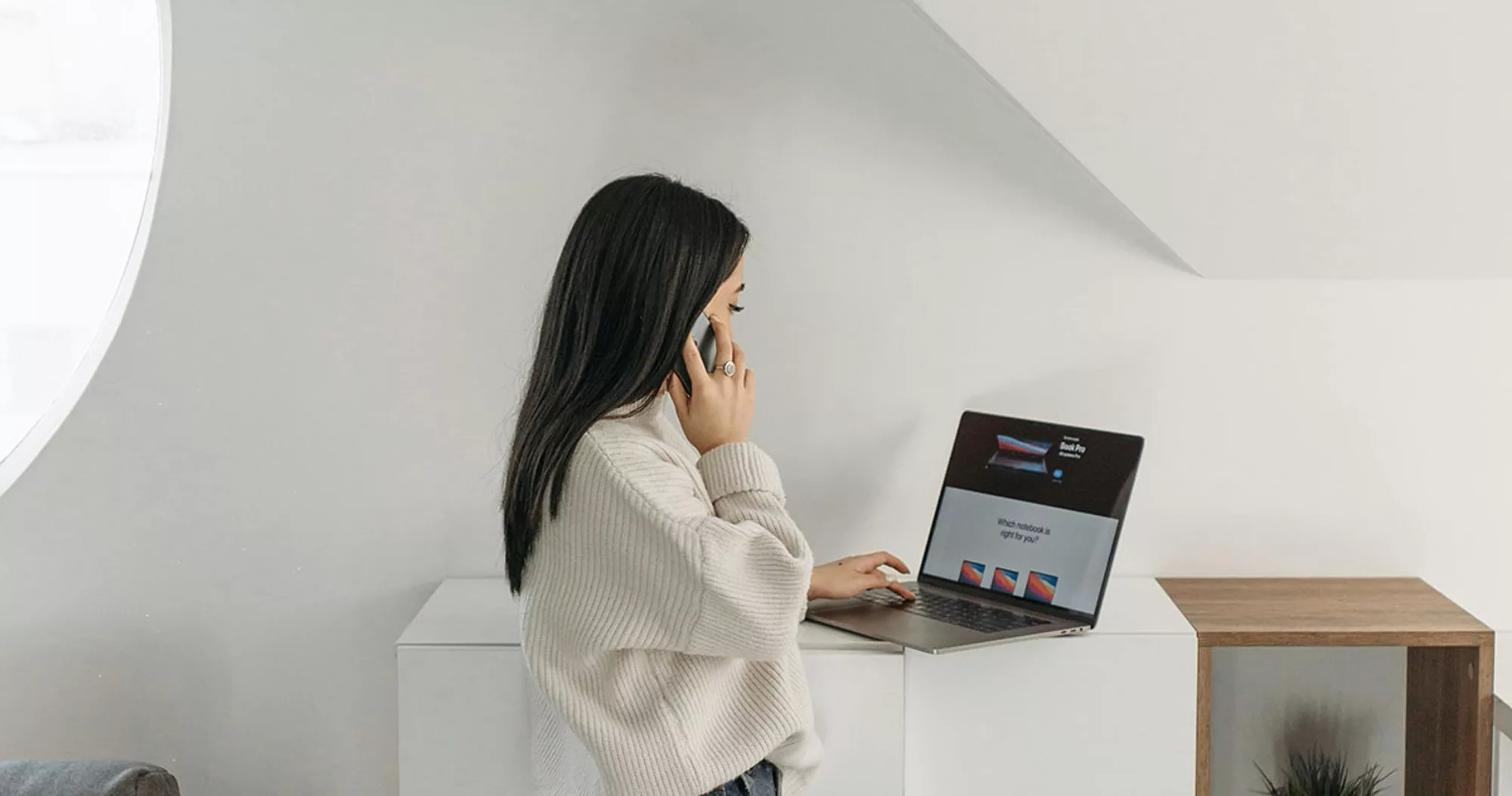 Woman working on a laptop while talking on the phone.