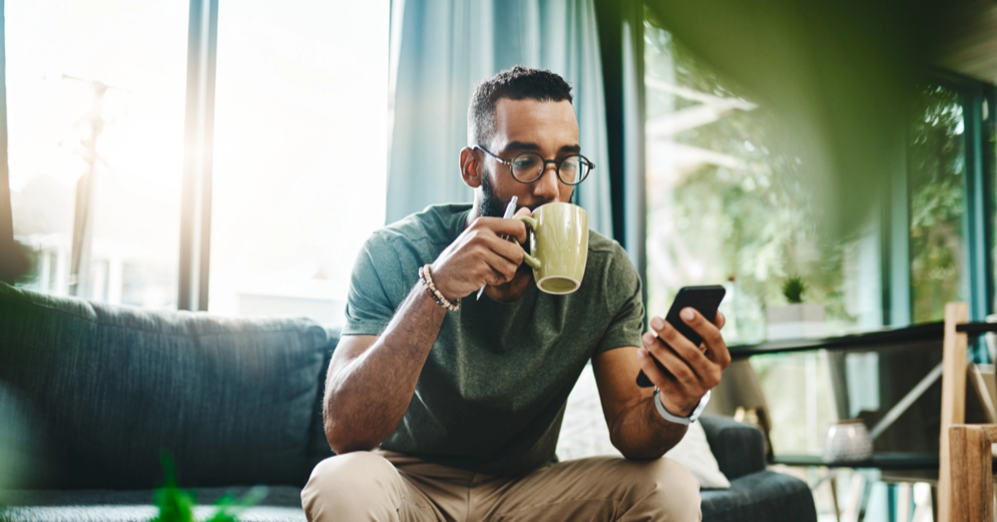 A man looking at his phone while drinking coffee