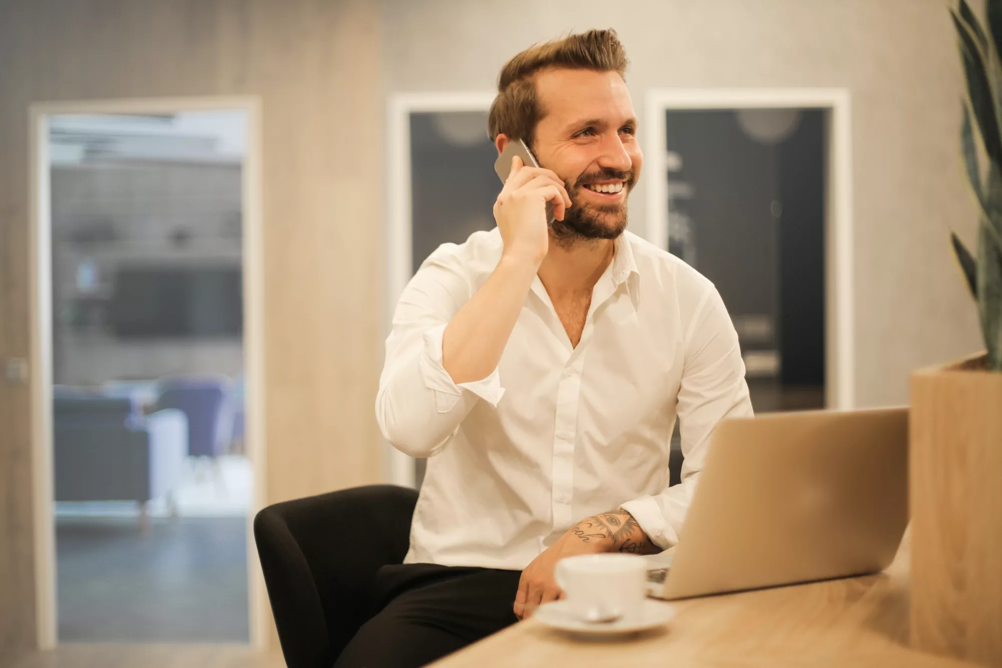 Smiling businessman talking on the phone while working on a laptop.