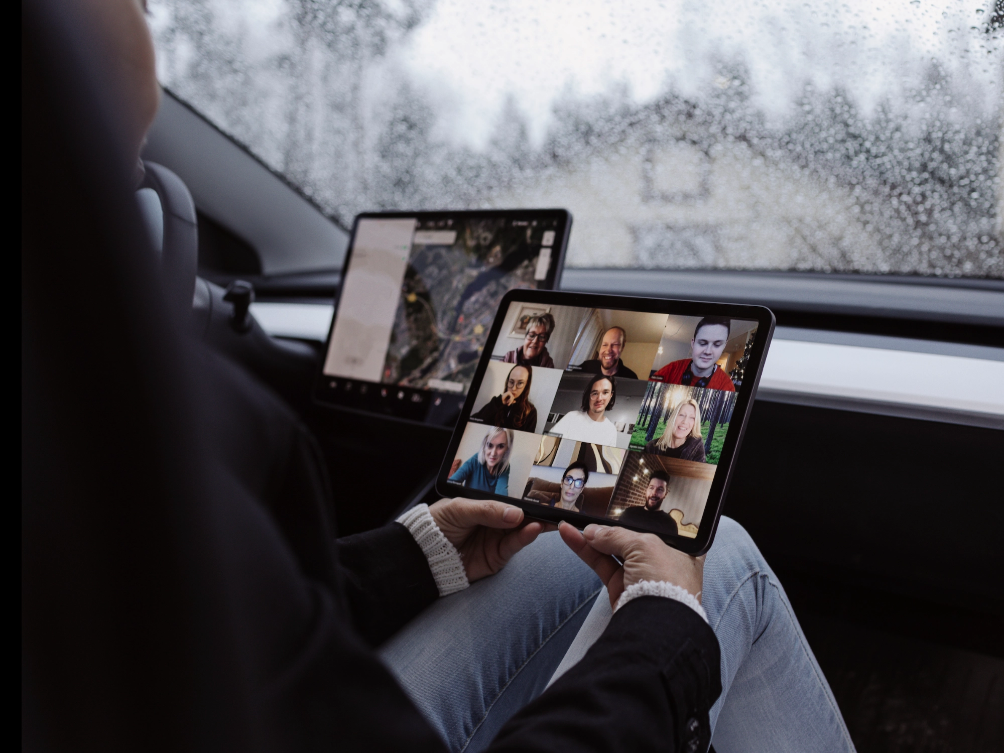 Person using a tablet for a video conference inside a car on a rainy day.