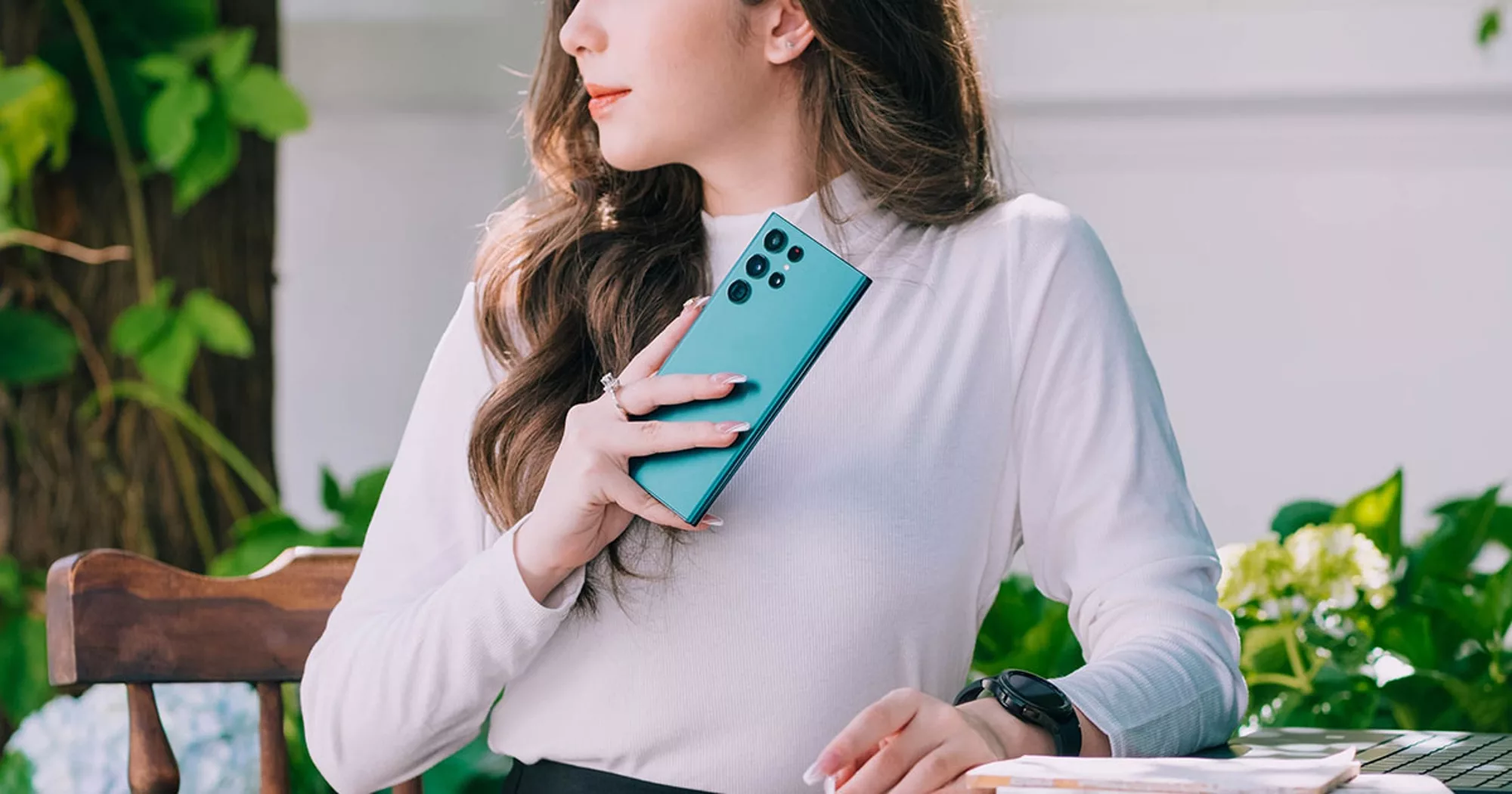 Woman holding a teal smartphone while sitting outdoors.